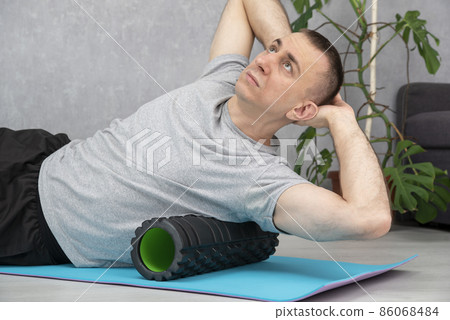 Man doing myofascial release of hyper-flexible muscles of back with massage foam roller. Workout at home. Self-massage of the back. 86068484