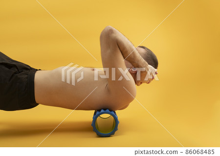 Sport man using myofascial roller for muscle and fascia stretching back. Handsome man doing exercises with foam roller. Side view 86068485