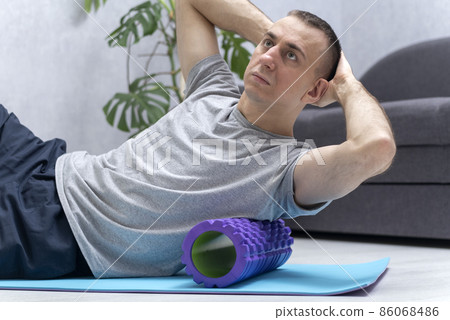 Man doing fascial exercise on side surface of back. Workout at home. Handsome man performs myofascial release massage of trigger points. 86068486