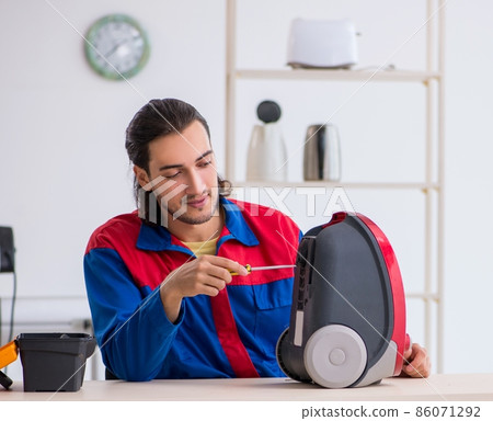 Young male contractor repairing vacuum cleaner at workshop 86071292