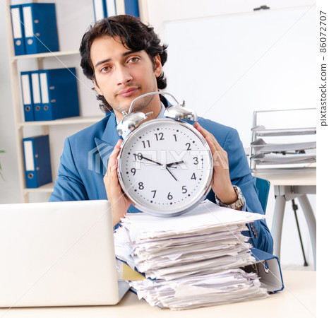 The young handsome male employee with too much work in the offic The young handsome male employee with too much work in the offic 86072707
