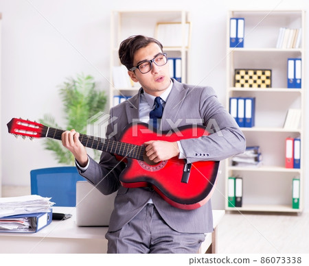 Young handsome businessman playing guitar in the office Young handsome businessman playing guitar in the office 86073338