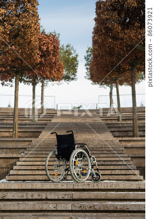 Wheelchair by the stairs without people outdoors.  86073921