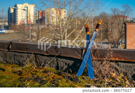 two crossed sharpened, sharp sabers, machetes stand on the roof of an abandoned building two crossed sharpened, sharp sabers, machetes stand on the roof of an abandoned building 86075027