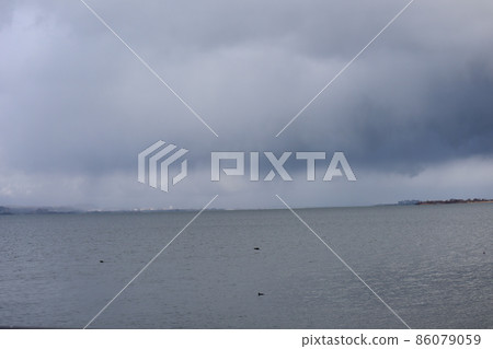 Lake Biwa on the surface of the lake with thick clouds and waterfowl, and the scenery of the cityscape on the opposite bank in the distance where it snows and blurs Lake Biwa on the surface of the lake with thick clouds and waterfowl, and the scenery of the cityscape on the opposite bank in the distance where it snows and blurs 86079059