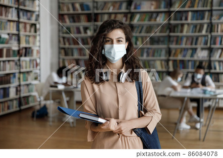Friendly student girl with wireless headphones wearing medical face mask Friendly student girl with wireless headphones wearing medical face mask 86084078