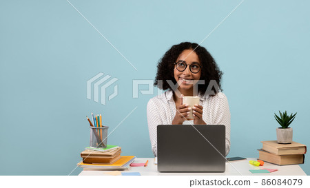 Happy black female sitting at desk with laptop and books, drinking coffee, having break during online studies or work Happy black female sitting at desk with laptop and books, drinking coffee, having break during online studies or work 86084079