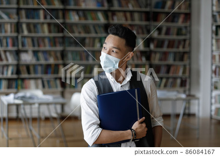 Thoughtful Asian college guy in mask visiting university campus library 86084167