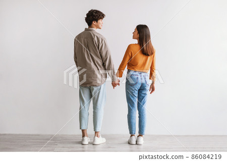 Full length of young Asian man and woman standing with their backs to camera, looking at each other and holding hands Full length of young Asian man and woman standing with their backs to camera, looking at each other and holding hands 86084219