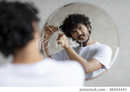 Male beauty care and hair problems. Sad indian man in white t-shirt can't comb hair, having pain and difficulties 86084442