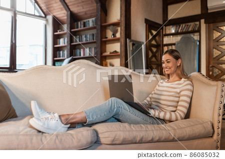 Smiling woman working on laptop at home 86085032