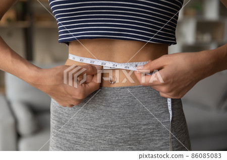 Close up sporty fit young woman measuring waist with tape. Close up sporty fit young woman measuring waist with tape. 86085083