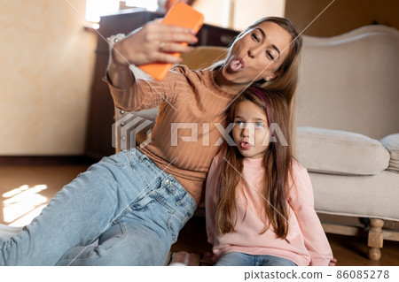 Portrait of smiling mom and daughter taking selfie using smartphone 86085278