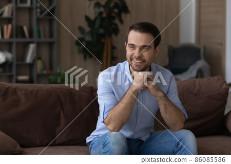 Smiling dreamy man sitting on couch, looking in distance 86085586