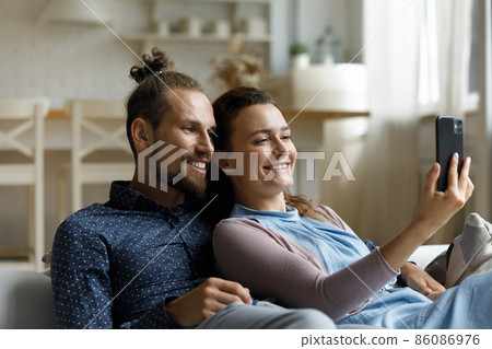 Joyful affectionate young family couple using cellphone at home. 86086976