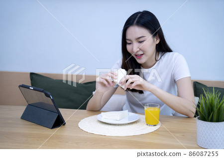 Asian woman eating breakfast with sandwiches and orange juice Asian woman eating breakfast with sandwiches and orange juice 86087255