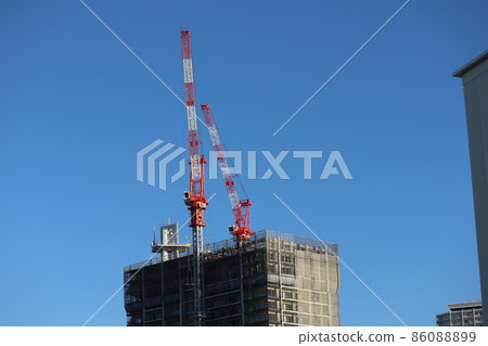 A view of the cityscape with a deep blue sky and a building under construction with two cranes carrying building materials 86088899