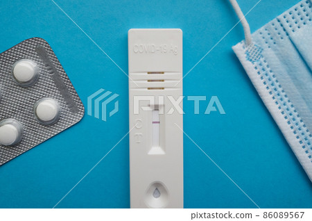Coronavirus antigen test with a negative result on a blue bright background next to a thermometer, a medical mask, pills and a syringe 86089567