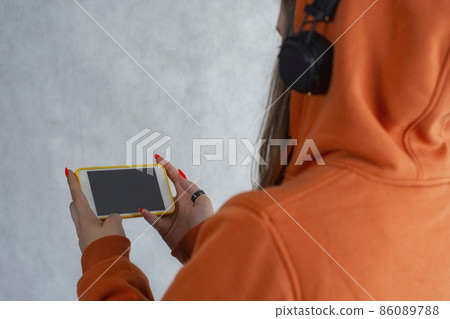 A girl in an orange sweater holds a smartphone in her hands A girl in an orange sweater holds a smartphone in her hands 86089788