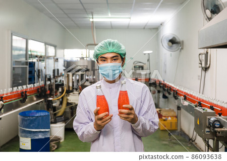 Asian man worker in sterile uniform showing product of bottled red juice in production line at beverage processing factory 86093638