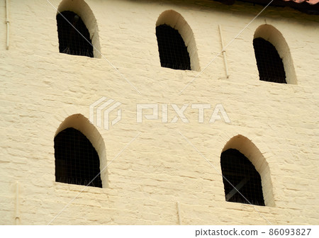 Dark window openings on the light whitewashed side of a historic church in Germany Dark window openings on the light whitewashed side of a historic church in Germany 86093827