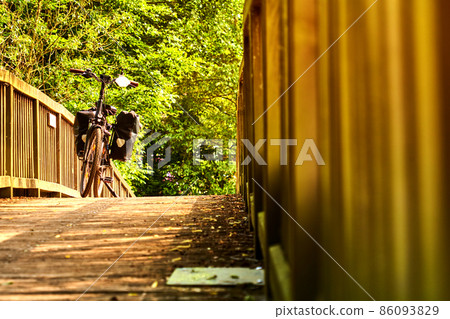 Black bicycle on a bike ride stands on a curved bridge made of wooden planks under a green canopy of leaves Black bicycle on a bike ride stands on a curved bridge made of wooden planks under a green canopy of leaves 86093829