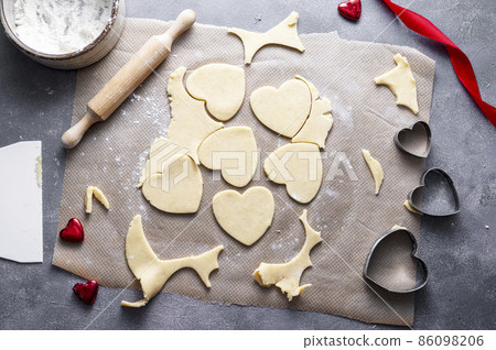 The process of cooking heart cookies. Top view of raw dough, rolling pin and baking cutters. Dark background 86098206