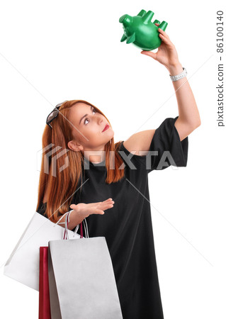 Redhead girl holding shopping bags and an empty piggy bank Redhead girl holding shopping bags and an empty piggy bank 86100140