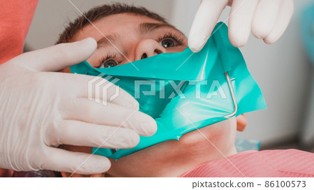 The dentist installs a rubber dam and a clamp for the treatment of a diseased tooth. The dentist installs a rubber dam and a clamp for the treatment of a diseased tooth. 86100573