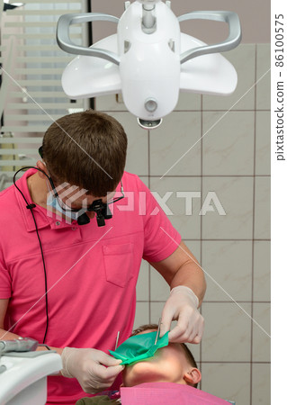 The dentist installs a rubber dam and a clamp for the treatment of a diseased tooth. The dentist installs a rubber dam and a clamp for the treatment of a diseased tooth. 86100575