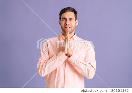 Portrait of excited young man holding hands folded in prayer beg about something make wish keep fingers crossed on pink isolated background in studio, looking at camera. Portrait of excited young man holding hands folded in prayer beg about something make wish keep fingers crossed on pink isolated background in studio, looking at camera. 86101382