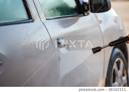 hand with high pressure washer washing white car at public self service car washing station 86102551