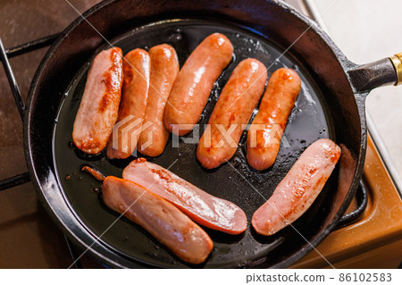half-cut sausages are fried in oil in a black cast iron skillet half-cut sausages are fried in oil in a black cast iron skillet 86102583