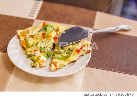 plate with slices of omelet of scrambled eggs with vegetables and stainless steel spatula plate with slices of omelet of scrambled eggs with vegetables and stainless steel spatula 86102670