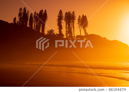 Bright sunrise with waves and rocks with trees. Joaquina beach in Brazil 86104874