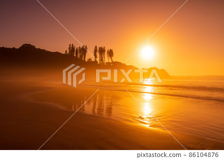 Bright sunrise with ocean waves and rocks with trees. Joaquina beach in Brazil 86104876