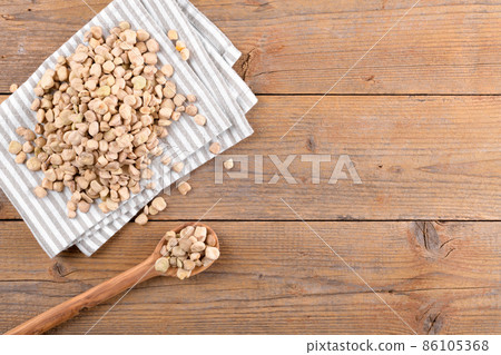 Dry raw cicerchia or indian pea on cotton napkin and in wooden spoon on natural wooden background, top view, copy space 86105368