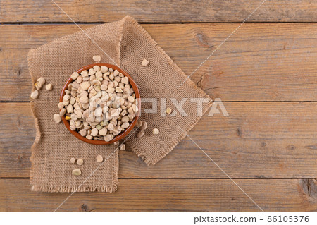 Dry raw cicerchia or indian pea on a clay plate with napkin on natural wooden background, top view, copy space. 86105376