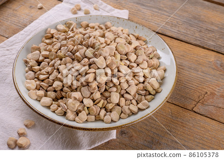 Dry raw cicerchia or indian pea on a ceramic plate with napkin on wooden background, close up 86105378