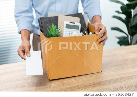 Resignation Concept The male officer standing, putting his box of his belongs on the desk and handing the white letter to someone Resignation Concept The male officer standing, putting his box of his belongs on the desk and handing the white letter to someone 86108427