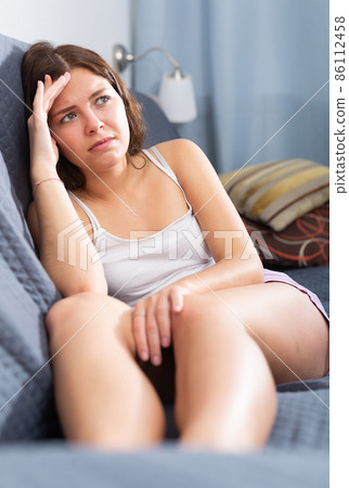 Upset girl sitting on sofa at home 86112458