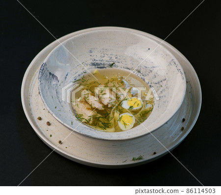 broth with noodles and quail egg in a white plate on a black background broth with noodles and quail egg in a white plate on a black background 86114503