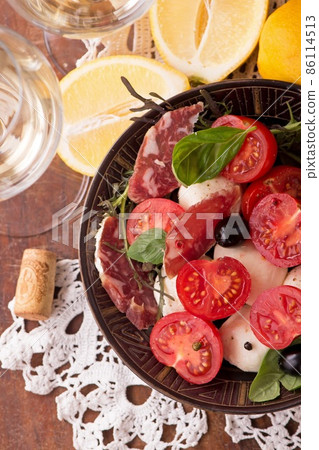 Organic Sugardrop tomatoes with basil and peppers, mozzarella cheese and sausage on a cutting board on a wooden table. 86114513