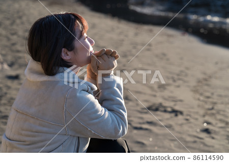 A woman staring at the winter sea where the setting sun pours A woman staring at the winter sea where the setting sun pours 86114590
