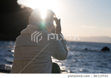 A woman staring at the winter sea where the setting sun pours A woman staring at the winter sea where the setting sun pours 86114591