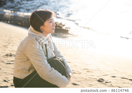 A woman staring at the winter sea where the setting sun pours 86114746