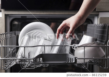 Close-up of female hand loading dished to, empty out or unloading from open automatic stainless built-in dishwasher machine with clean utensils inside in modern home kitchen. Household domestic life 86115239