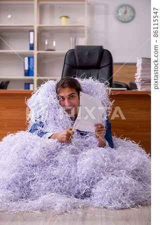 Young male employee and a lot of cut papers in the office Young male employee and a lot of cut papers in the office 86115547