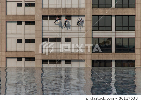 Group of workers cleaning windows service on high rise office building with reflection fiom swimming pool. 86117538