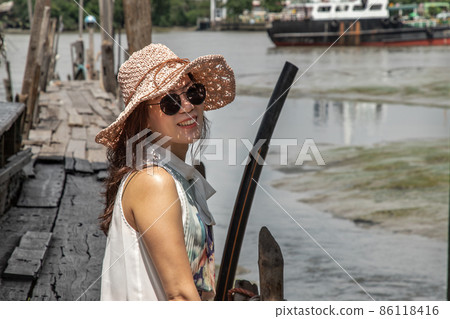 The girl in casual clothes are sitting smiling happily on the old wooden pier by the river. The girl in casual clothes are sitting smiling happily on the old wooden pier by the river. 86118416